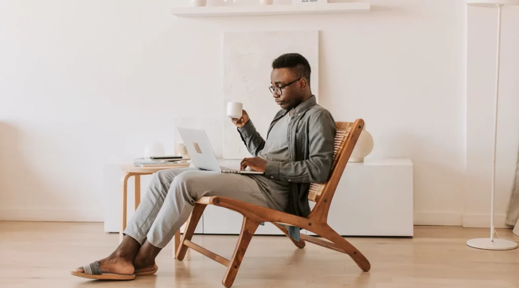 Mann sitzt auf stuhl mit Kaffeetasse und Laptop