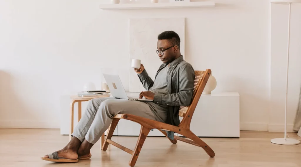 Mann sitzt auf Stuhl mit Kaffeetasse und Laptop