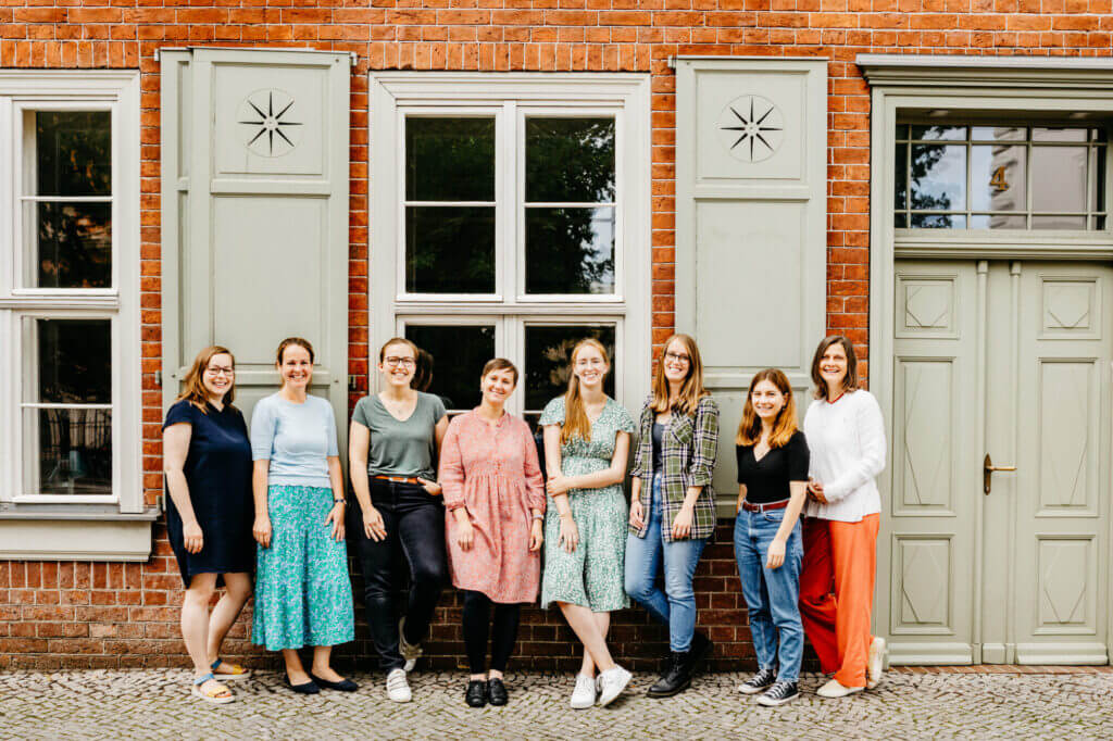 Team von Fjordkind-Reisen. Acht Frauen, die vor einer Wand stehen und in die Kamera lächeln.